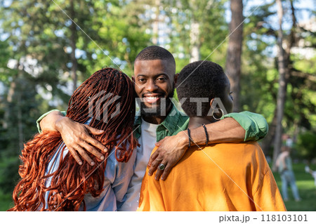 Smiling African American man hugs friends girls who standing with their backs to camera. Friendship Smiling African American man hugs friends girls who standing with their backs to camera. Friendship 118103101