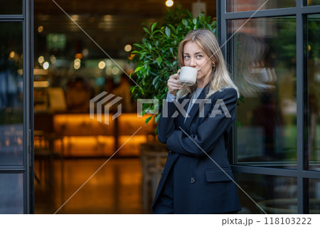 Confident pleased middle aged businesswoman drinks morning coffee standing at entrance of coffeeshop Confident pleased middle aged businesswoman drinks morning coffee standing at entrance of coffeeshop 118103222