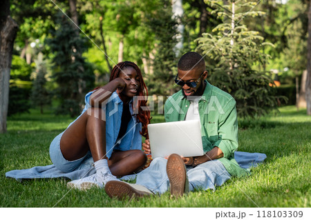 Busy black couple of students engaged with laptop, viewing movies, and browsing web in park Busy black couple of students engaged with laptop, viewing movies, and browsing web in park 118103309