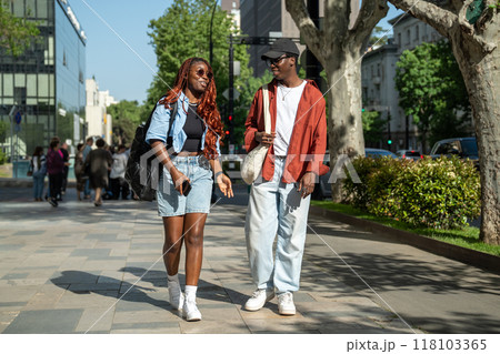 Contented African American young couple happily walks downtown chatting smiling enjoy sunny weather. Contented African American young couple happily walks downtown chatting smiling enjoy sunny weather. 118103365