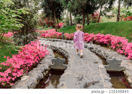 Little girl in pink dress walk in summer garden with blooming azalea flowers. Little girl in pink dress walk in summer garden with blooming azalea flowers. 118108843