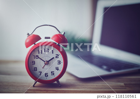 開いたノートパソコンと赤い目覚まし時計 118110561