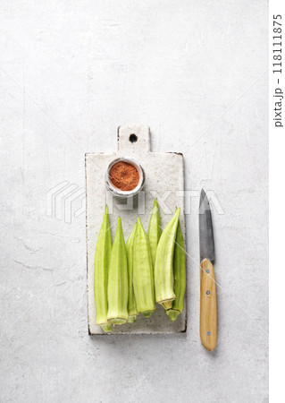 Bamya or okra on cutting board with knife and paprika on gray background, top view, copy space Bamya or okra on cutting board with knife and paprika on gray background, top view, copy space 118111875