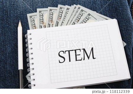 STEM word and symbols on a checkered notebook against the background of American paper bills STEM word and symbols on a checkered notebook against the background of American paper bills 118112339