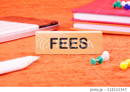 Business and finance concept. Costs, charges, commissions, penalties. Cost, fee and taxes. FEES on a wooden bar in front of an orange background, front view Business and finance concept. Costs, charges, commissions, penalties. Cost, fee and taxes. FEES on a wooden bar in front of an orange background, front view 118112347