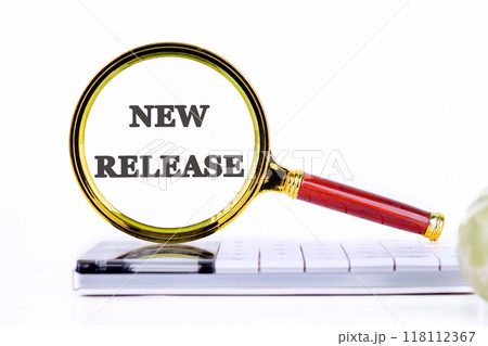 New Release written through a magnifying glass, close-up on a calculator in front of a light background 118112367