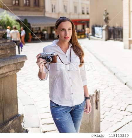 Woman holding a camera walking through a historic street on a sunny day in a European city Woman holding a camera walking through a historic street on a sunny day in a European city 118113839