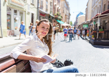Young woman sitting on the bench in an old city and reading book on sunny day 118113846
