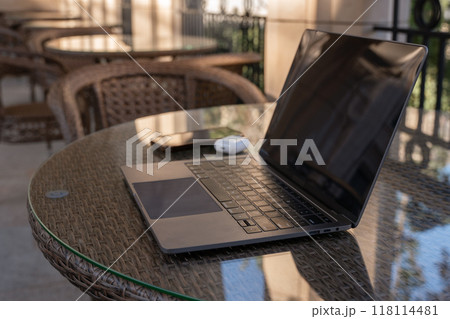 Laptop, Phone, Table - Open laptop, cell phone, and mouse on a table in a cafe setting. Laptop, Phone, Table - Open laptop, cell phone, and mouse on a table in a cafe setting. 118114481