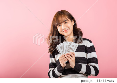 Asian happy portrait beautiful young woman smiling holding money fan banknotes 100 dollar bills isolated on pink background Asian happy portrait beautiful young woman smiling holding money fan banknotes 100 dollar bills isolated on pink background 118117983