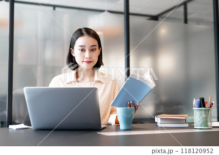 本を参考にしながらパソコンを使用して作業をしている女性 本を参考にしながらパソコンを使用して作業をしている女性 118120952