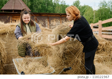 Two Women Gathering Hay Outdoors on Sunny Day Two Women Gathering Hay Outdoors on Sunny Day 118122367