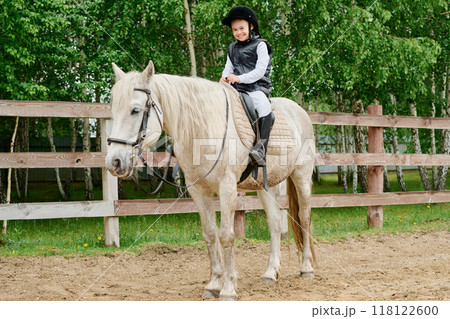 Smiling Girl Riding White Horse in Paddock 118122600
