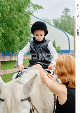 Boy Riding Horse with Assistance of Trainer Outdoors 118122626