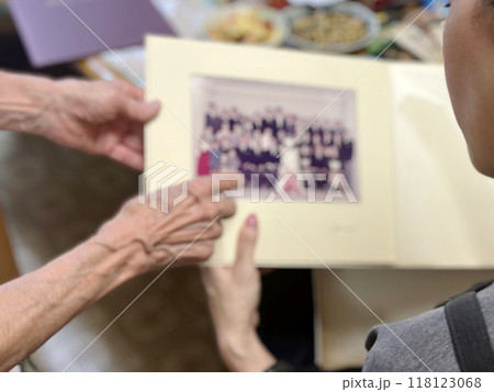 結婚式の集合写真を指さす高齢女性の手と若い女性の後姿 118123068