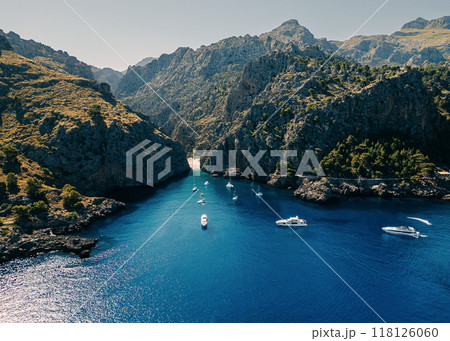 Aerial view of yachts and boats anchored in a secluded bay surrounded by towering rocky cliffs Aerial view of yachts and boats anchored in a secluded bay surrounded by towering rocky cliffs 118126060