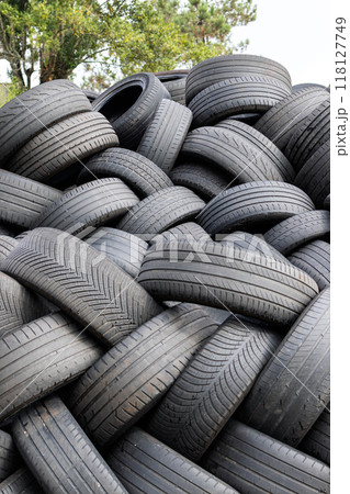 A large stack of used car tires waiting to be recycled, with a tree in the background. A large stack of used car tires waiting to be recycled, with a tree in the background. 118127749