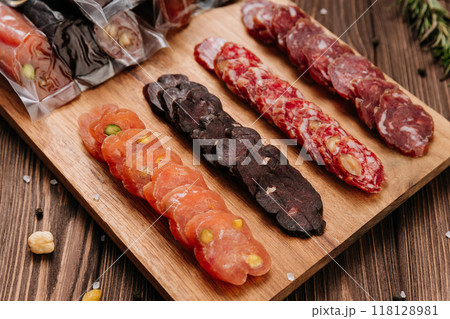 Sliced sausage with pistachios on wooden board, ideal for food presentations and gourmet displays Sliced sausage with pistachios on wooden board, ideal for food presentations and gourmet displays 118128981