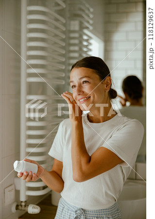 A woman is applying her skincare routine in a beautifully designed modern bathroom space A woman is applying her skincare routine in a beautifully designed modern bathroom space 118129637