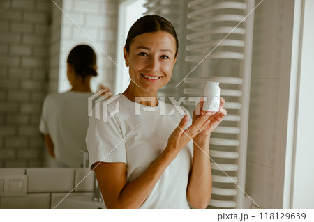 A woman enthusiastically promoting a skincare product in a stylish and modern bathroom setting 118129639