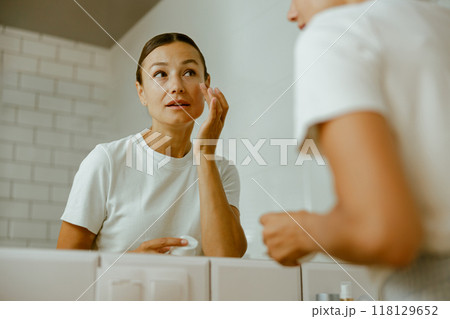 A woman applying skincare in a modern bathroom shows a calming beauty and selfcare routine 118129652