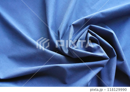 Abstract background with blue fabric twisted in a spiral. Cotton textile, folds, rays diverge to the edges. Top view, close-up, copy space. 118129990