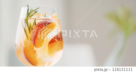 A close-up of a refreshing peach spritzer in a glass, garnished with fresh rosemary and ice cubes 118131111