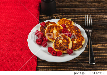 Cottage cheese pancakes with fresh raspberries on a white plate on the table Cottage cheese pancakes with fresh raspberries on a white plate on the table 118132952