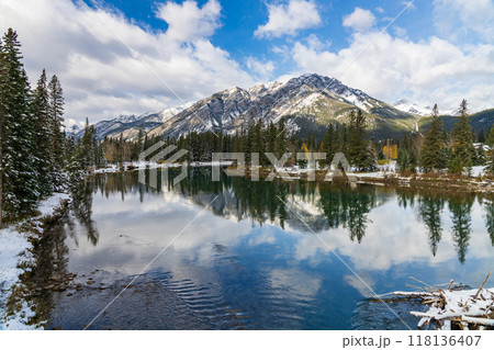 Banff National Park beautiful natural scenery in winter sunny day. Mount Norquay with blue sky, white clouds reflected on Bow River like a mirror. Town of Banff, Canadian Rockies. 118136407
