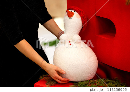 Happy Snowman image wears winter clothes and festive green branches of fir tree are in a room with white curtains on a window. Concept: Christmas and New Years holidays card. Happy Snowman image wears winter clothes and festive green branches of fir tree are in a room with white curtains on a window. Concept: Christmas and New Years holidays card. 118136996
