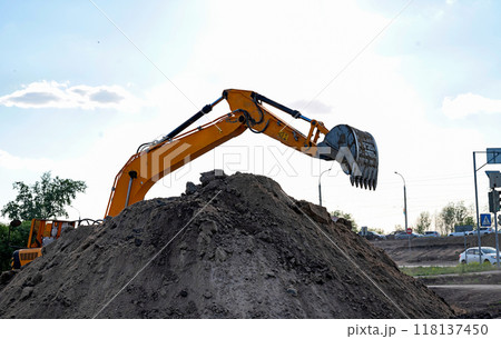 Excavator during earthmoving at open pit on blue sky background. Construction machinery and earth-moving heavy equipment for excavation, loading, lifting and hauling of cargo on job sites Excavator during earthmoving at open pit on blue sky background. Construction machinery and earth-moving heavy equipment for excavation, loading, lifting and hauling of cargo on job sites 118137450
