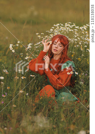A shepherdess woman with red hair and a green dress sits in a field of flowers. A shepherdess woman with red hair and a green dress sits in a field of flowers. 118138038