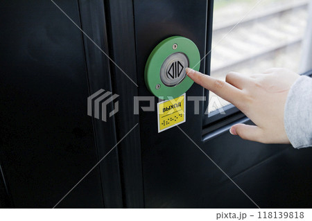 A person is pressing a green button located on a door surface, the inscription in Russian is the exit A person is pressing a green button located on a door surface, the inscription in Russian is the exit 118139818
