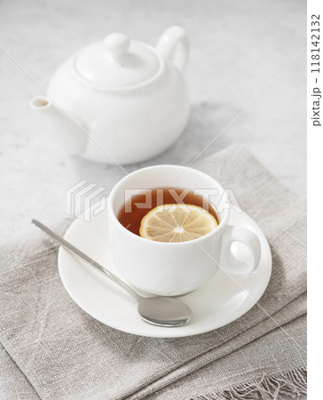 Tea with lemon in a white cup on a light background with  a teapot.  118142132