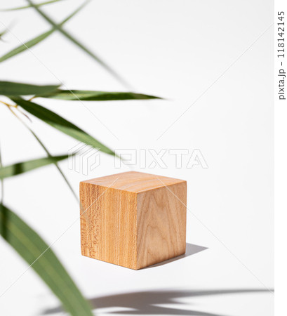 Empty wooden cube with shadows and green leaves on a white background. Empty wooden cube with shadows and green leaves on a white background. 118142145