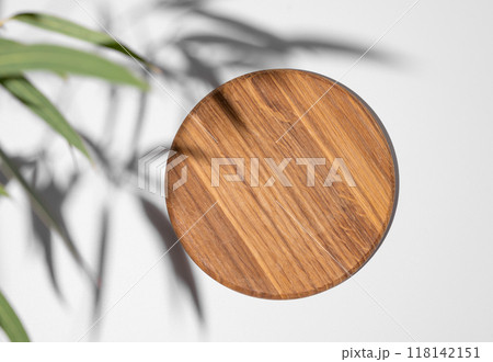 Wooden empty round board with green leaves  on a white background with shadows. 118142151