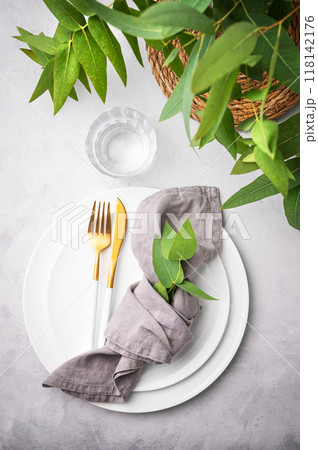 Festive table setting with white plates and cutlery on a light background with napkin and eucalyptus Festive table setting with white plates and cutlery on a light background with napkin and eucalyptus 118142176