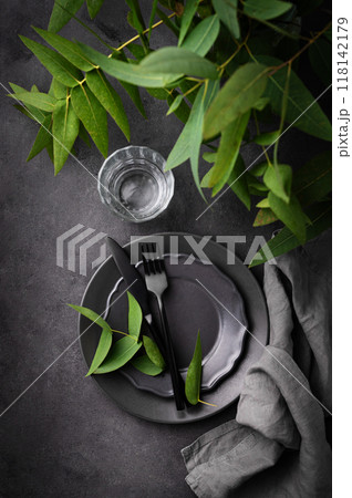 Table setting with a dark gray plates, a glass  and a napkin with eucalyptus branches  118142179