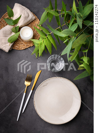 Table setting with a empty beige plate, a glass, a candle and a napkin with eucalyptus branches Table setting with a empty beige plate, a glass, a candle and a napkin with eucalyptus branches 118142274