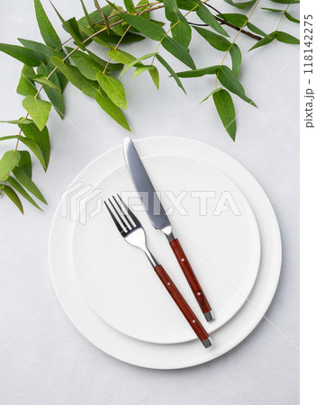 Festive table setting with white plates and cutlery on a light background with eucalyptus branches. 118142275
