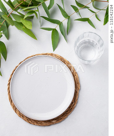 Table setting with a blue plate and a glass on a straw napkin with eucalyptus branches  118142284