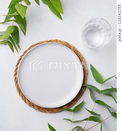 Table setting with a blue plate and a glass on a straw napkin with eucalyptus branches  118142285