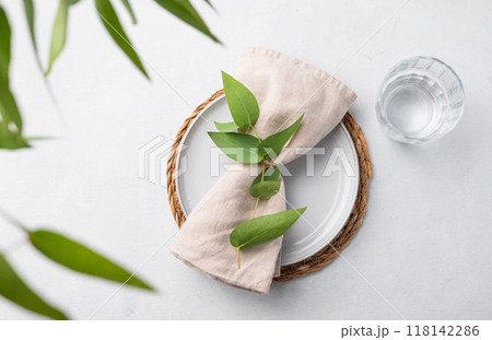Table setting with a blue plate and a glass on a straw napkin with eucalyptus branches  118142286