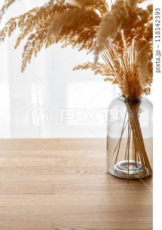Stylish modern dry herb in a glass vase on a wooden background opposite a window 118142393