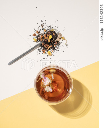 Creative flat lay of a glass cup of herbal tea with rose flowers on a yellow and white background  118142398