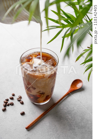 Iced coffee latte in a tall glass with a hand pouring milk from a milk jug on a light background Iced coffee latte in a tall glass with a hand pouring milk from a milk jug on a light background 118142405