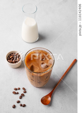 Vegan iced coffee latte in a tall glass with soy milk on a light background with coffee beans  118142406