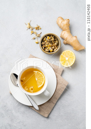 Chamomile herbal tea with lemon in a white cup on a light background with dry flowers and ginger. Chamomile herbal tea with lemon in a white cup on a light background with dry flowers and ginger. 118142408