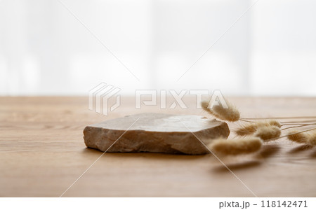 A beige stone slab on a wooden tabletop in front of a window with dried flowers. 118142471