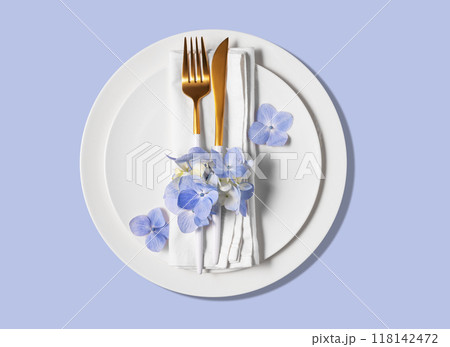 Festive table setting with blue hydrangea flowers and white plates on a blue background. Festive table setting with blue hydrangea flowers and white plates on a blue background. 118142472
